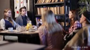 一群快乐的青少年朋友在艺术咖啡馆吃午餐时坐在桌子边聊天，服务员<strong>正在</strong>端咖啡